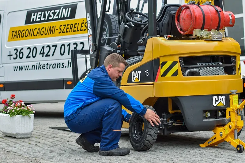 Szerelő tömör gumit szerel Cat targoncára a szervizautó mellett